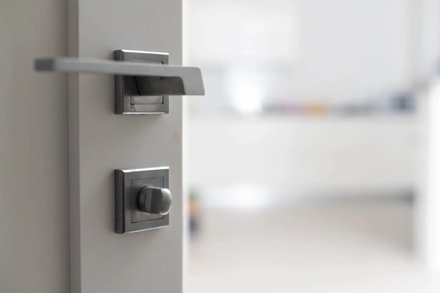 Béquille en acier brossé et bouton de condamnation d'une porte d'entrée entrebâillée dans un appartement de standing du Champ-de-Mars